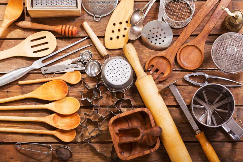  A variety of kitchen utensils made of wood and metal are arranged on a wooden table.